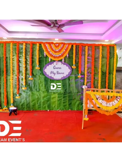 A simple yet beautiful naming ceremony setup featuring a backdrop of fresh banana leaves and a cradle decorated with marigold garlands. This is perfect for a traditional ceremony at home.