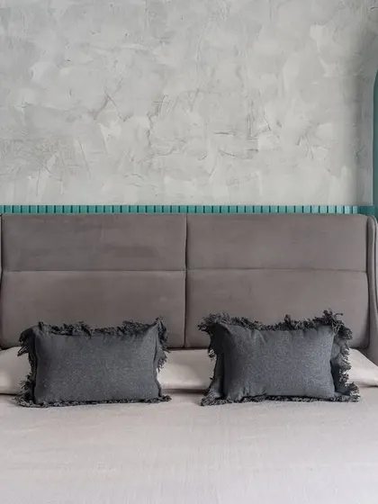 For one of the matriarchs' rooms, I juxtaposed a rugged concrete texture wall with vibrant teal details. The arched dressing mirror and upholstered headboard soften the industrial feel.