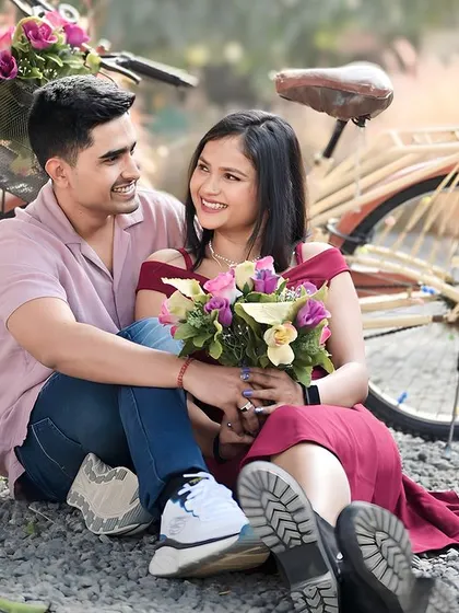 A sweet couple portrait with a vintage bicycle prop, set against a backdrop of tall grass. The flowers in the basket add a pop of color and romance to this outdoor engagement photo.