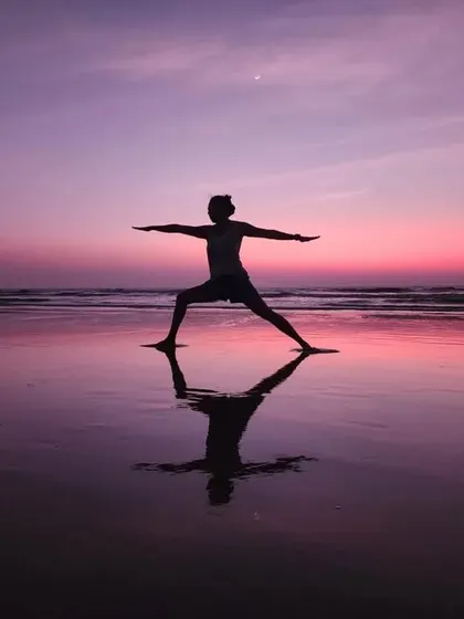 The classic Virabhadrasana II (Warrior II) pose, captured beautifully by a student on the beach at sunset. The reflection on the wet sand doubles the beauty and power of the moment.