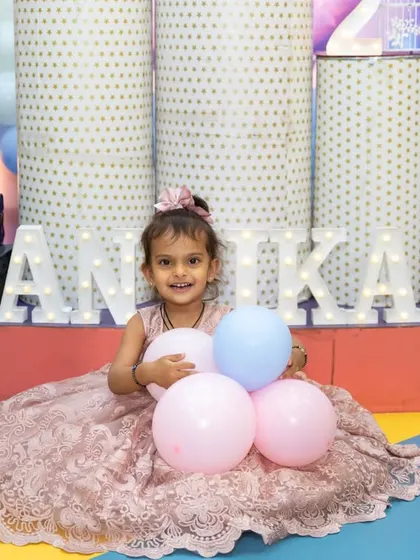 A smiling birthday girl in a beautiful lace dress, holding balloons. This portrait captures the sweet innocence and happiness of childhood celebrations.