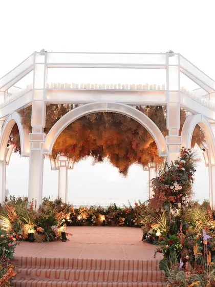 The ethereal mandap structure stands against the open sky, adorned with florals in sunset shades, ready for a magical ceremony by the ocean.