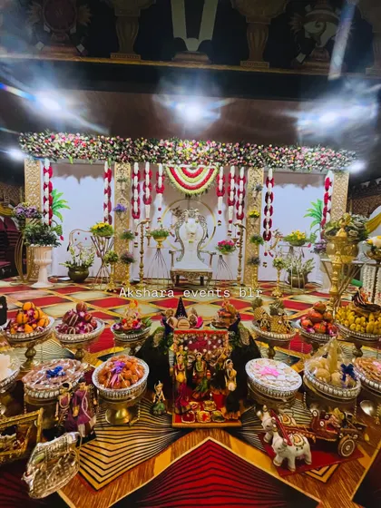 A beautifully lit Seemantham stage at night, showcasing the main stage, ornate chair, and a lavish display of traditional offerings. The red and white floral hangings create a classic and festive look.