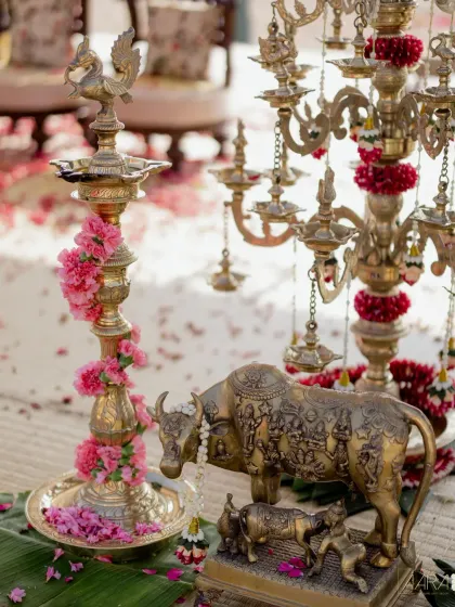 Traditional brass artifacts, including a Nandi statue and a multi-tiered lamp, are adorned with fresh flowers. These sacred elements are central to creating an authentic and spiritual wedding ambiance.