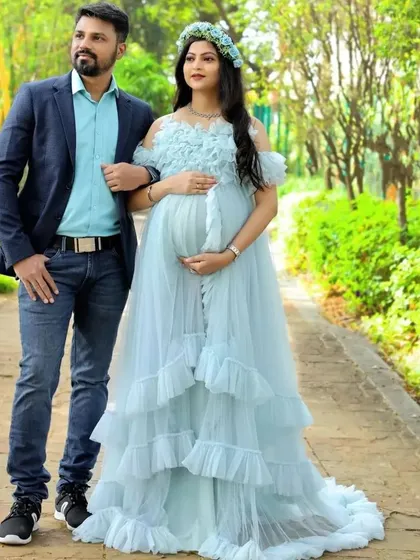 A classic couple's pose featuring our light blue ruffled gown. This dress is a popular rental for its romantic style and beautiful color, perfect for outdoor maternity photography.