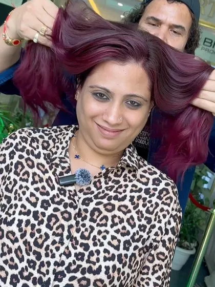 A happy client showing off her new, luscious wine-toned hair, a truly bold and vibrant choice.