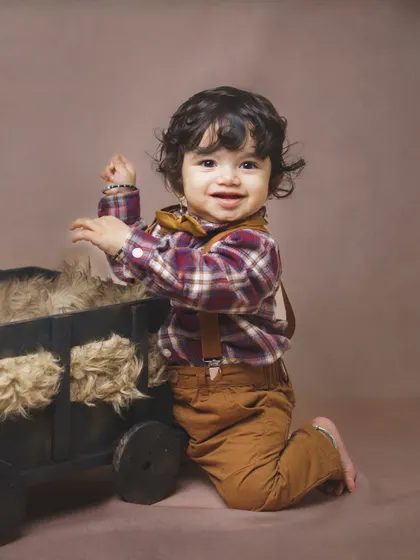 Ready for an adventure! This little boy's happy expression is perfectly captured as he plays with a wooden cart prop during his indoor baby photoshoot.