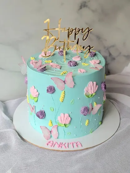 A simple floral cake in pretty pastel colors. The light blue buttercream is decorated with piped flowers and delicate butterflies.