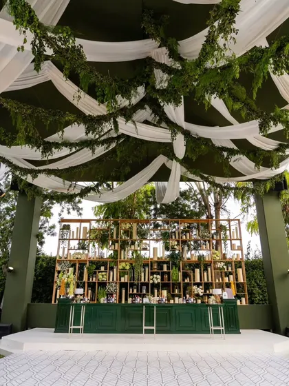 The centerpiece of this anniversary party was the bar. I designed a custom green bar with a stunning back-shelf display, all set under a ceiling of draped white fabric and hanging greenery.