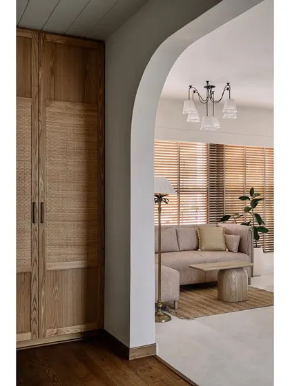 A view through an archway into the guest bedroom, showcasing the warm, cottage-inspired design with woven and wooden textures.