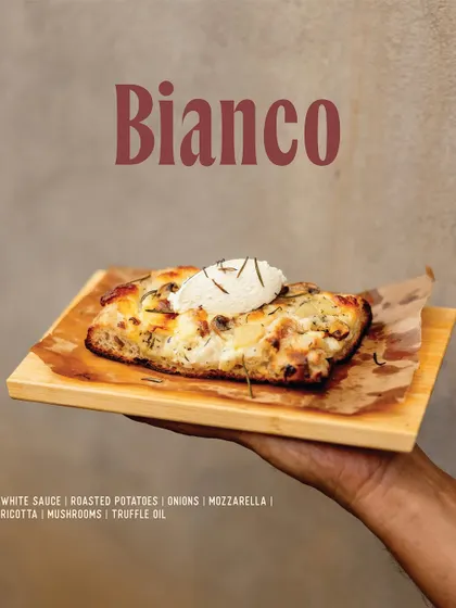 The Bianco Pizza Romana. This white pizza features a base of white sauce, roasted potatoes, onions, mushrooms, mozzarella, and a final dollop of fresh ricotta and truffle oil.