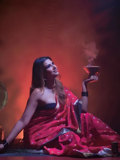 An artistic, full-length portrait of a model in a red saree, seated next to a gramophone with smoke creating a mystical atmosphere.