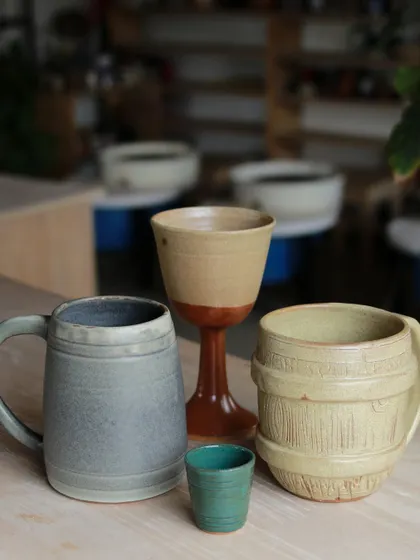 A showcase of drinkware created by our professional program students, including a large beer mug, a goblet, and a barrel shaped mug, demonstrating their skill in creating diverse and functional forms.