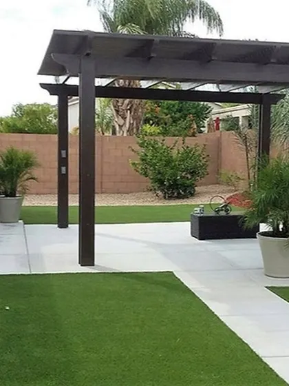 This landscape features a combination of artificial grass and a concrete patio, with a dark-stained wooden pergola defining the outdoor living space.