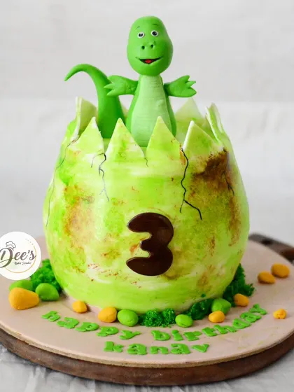 The big reveal. A cute, friendly dinosaur pops out of the cracked egg, all made from cake and fondant.