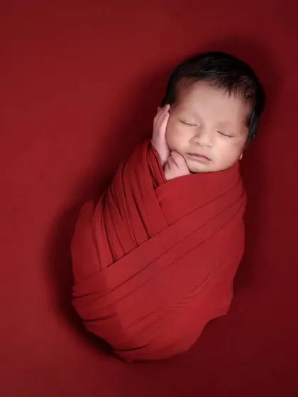 A simple and powerful newborn portrait. The baby is swaddled snugly in a bold red wrap against a matching background, creating a striking and minimalist image.