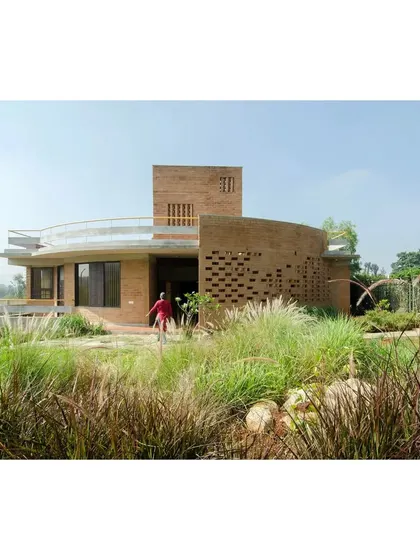 The "Breathe" house featured in a publication, with the iconic curved jaali wall and surrounding native grasses in the foreground.