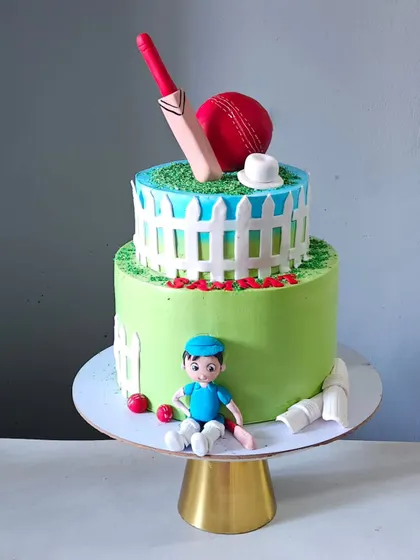 A fun cricket-themed cake for a sports lover. This two-tiered design features a cricket pitch on top with an edible bat and ball, and a cute, handcrafted cricketer figurine at the base.
