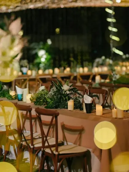 A shot of the long dining tables being set up for an elegant welcome dinner under fairy lights.