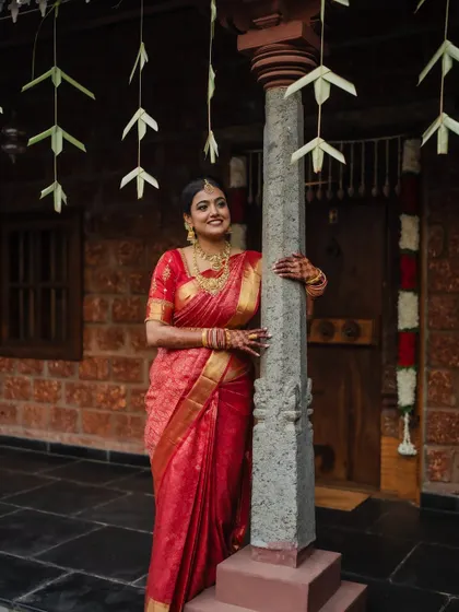 A portrait of the bride in her stunning red saree, framed by the rustic charm of her wedding venue. We focus on creating images that are both beautiful and full of character.