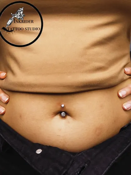 A classic navel piercing featuring a simple, elegant crystal barbell. This close-up shows the clean placement and precision I aim for with every body piercing.