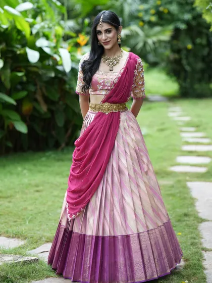 A beautiful Kanchipuram silk half saree in shades of pink and gold. The look is completed with a pre-draped dupatta, offering a modern and hassle-free take on a traditional outfit.