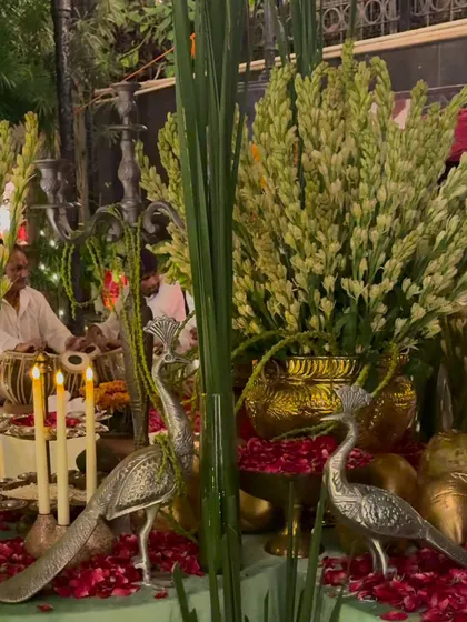 Silver peacock statues and candles are placed amongst arrangements of tuberose, adding a touch of elegance and traditional symbolism to the decor for the spiritual gathering.
