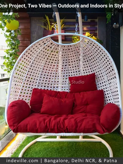 A comfortable and vibrant balcony seating solution. This large white wicker swing chair with bright red cushions provides a perfect spot to relax, surrounded by a vertical garden and hanging plants.