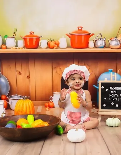 A happy baby playing with toy vegetables during the nine-month chef milestone session.