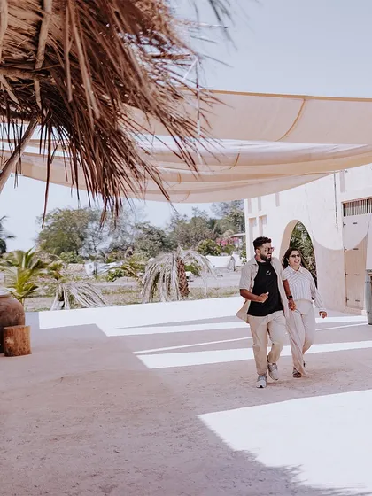 A wide shot of a couple walking hand-in-hand through a beautiful, sunlit resort, perfect for a destination pre-wedding feel.