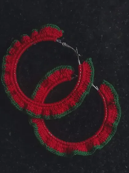 These crochet hoop earrings feature a festive red and green frilly edge. They are a fun and lightweight accessory, perfect for holiday parties or adding a pop of color.