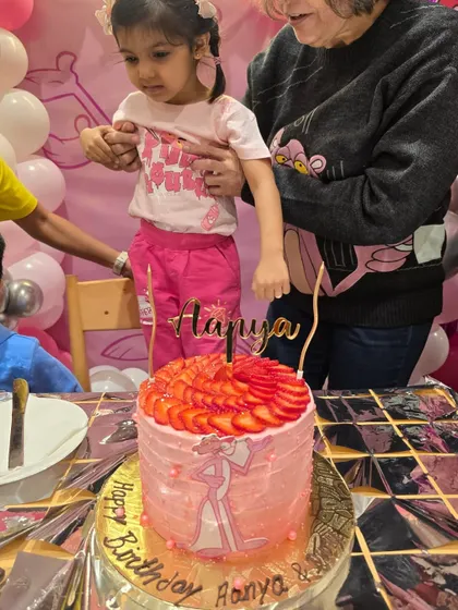 A Pink Panther-themed birthday for little Aanya. Her custom cake features pink frosting and a fresh strawberry topping to match the party's fun theme.