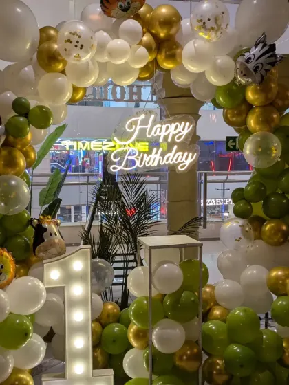 A classic jungle theme for a first birthday party. The green, white, and gold balloon arch is decorated with cute animal foil balloons and a light-up number '1' for a wild celebration.