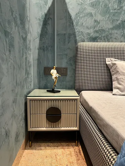 A close-up of a custom bedside table with fluted drawer fronts and a glass top. The houndstooth pattern of the bed upholstery adds a classic touch to this modern bedroom in Ambala.