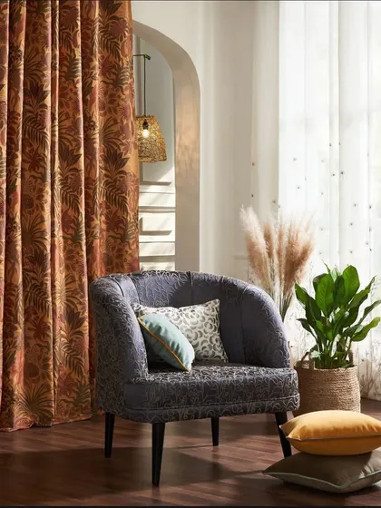 A cozy corner featuring an armchair upholstered in a rich, dark fabric. The warm tones of the curtains and the natural elements like pampas grass create an inviting and stylish vignette.