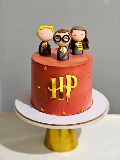 A minimalist yet magical Harry Potter cake. This airbrushed whipped cream cake features the iconic HP logo and cute, stylized figurines of Harry, Ron, and Hermione.