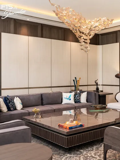 This living room is defined by its rich textures and layered design. A large, comfortable sectional sofa is paired with a substantial stone-topped coffee table. The wall paneling combines wood and lighter tones, creating a sophisticated backdrop for the custom furniture and dramatic overhead light fixture.