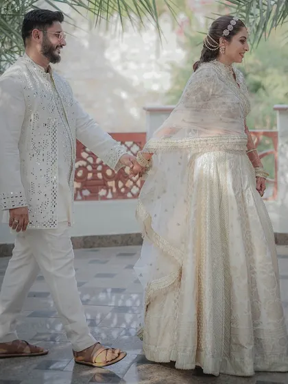 A candid shot of the couple walking hand-in-hand, their elegant white outfits creating a serene and classic look for their pre-wedding ceremony.