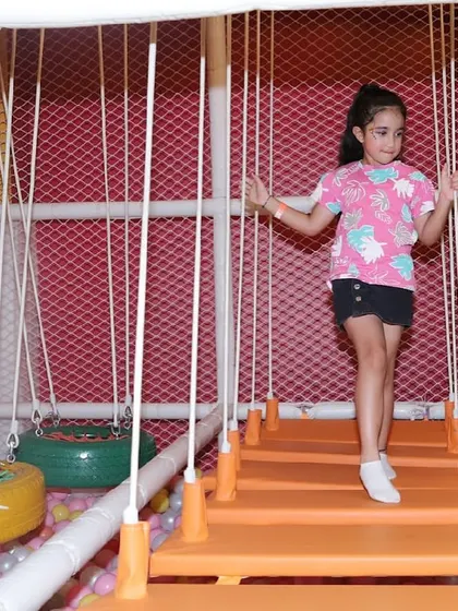 A girl carefully makes her way across a suspended rope bridge in our soft play jungle gym.