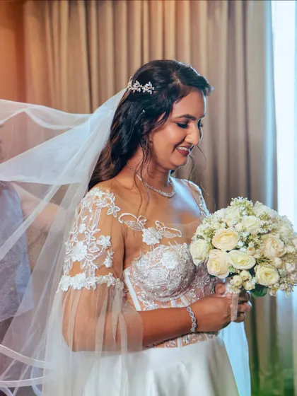 A happy bride holding her bouquet. The veil gently frames her face, highlighting her radiant smile and glowing makeup.