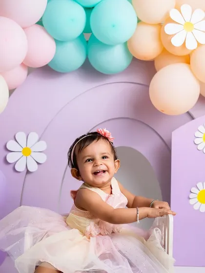 A moment of pure happiness amidst a field of pastel daisies and balloons. Her joyful smile is the centerpiece of this beautiful, custom-designed first birthday set.