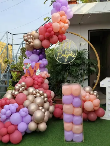 A modern and stylish outdoor decoration for a first birthday. I created an asymmetrical balloon garland on a circular gold frame, using a vibrant mix of pink, purple, and orange balloons, complemented by a light-up number '1'.