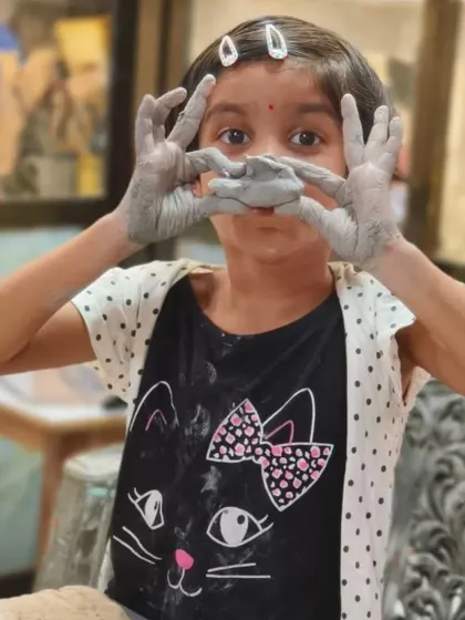 A young artist playfully peeks through her clay-covered hands. Our classes for kids are all about encouraging self-expression and having fun with the creative process.