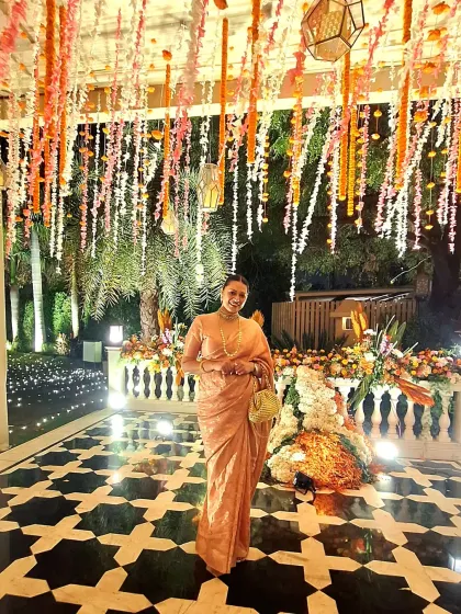 Attending a wedding celebration in a timeless peach-toned saree. The simplicity of the drape is elevated by a classic pearl necklace and a handcrafted bag, proving that elegance often lies in understated details.