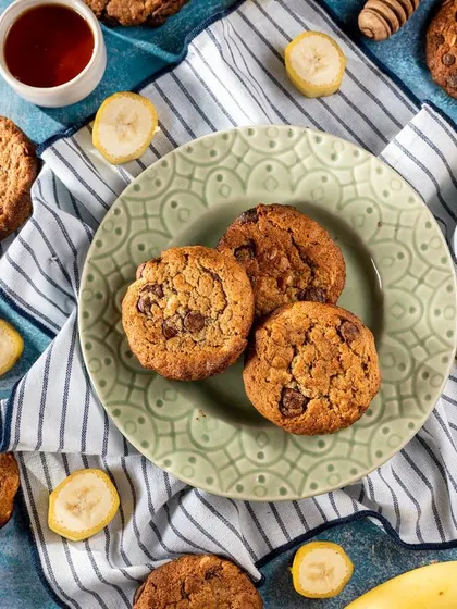 A creative flat lay of freshly baked cookies for Siaa Desert Bakery. The cookies are arranged on a plate and scattered with ingredients like banana slices and chocolate chips, creating a playful and delicious composition.