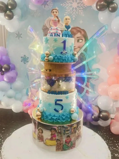 A magical Frozen-themed butterfly cake celebrating two birthdays in one. This design features Anna and Elsa toppers, the numbers '1' and '5', and a base wrapped in cherished family photos.