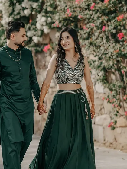 A romantic portrait of a couple, hand in hand, walking through a garden, their coordinated green outfits perfect for a Mehendi function.