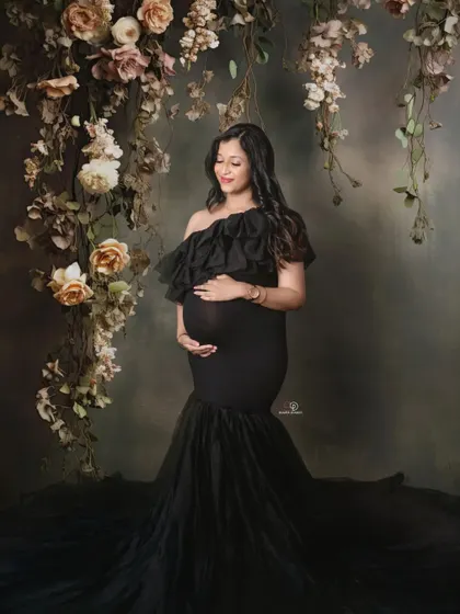 A classic and moody portrait with a beautiful mom-to-be in a black ruffled gown against a floral backdrop. This style is perfect for a timeless and dramatic maternity photo.