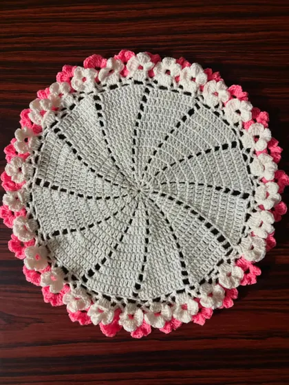 A clear, top-down photo of the white and pink pinwheel doily, highlighting the detailed stitch work.