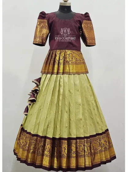 A unique color combination of a maroon peplum top with a light green pleated skirt. The top features traditional zari work on the sleeves, matching the border of the skirt.